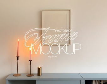 May include: A white picture frame mockup with a 4x5 ratio, hanging on a light beige wall. Two lit candles on metal candle holders and a gold candle are on a grey shelf below the frame.