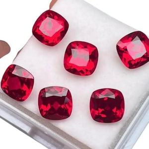May include: Six red cushion-cut gemstones in a white box. The gemstones are all the same size and shape.