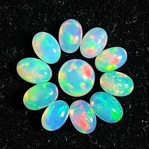 May include: A collection of opals with a vibrant play of color. The opals are oval-shaped, with a mix of blue, green, and red hues. The opals are arranged on a black surface, showcasing their iridescent qualities. The central opal is round.