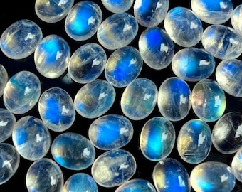 May include: A collection of oval-shaped moonstone cabochons with iridescent blue and white colors. The stones are smooth and polished, with a translucent appearance.