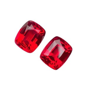 May include: Two red cushion-cut gemstones. The gemstones are faceted and have a high polish.