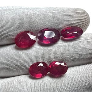 May include: Five oval-shaped, faceted ruby gemstones. The rubies are a deep red color and have a high polish.