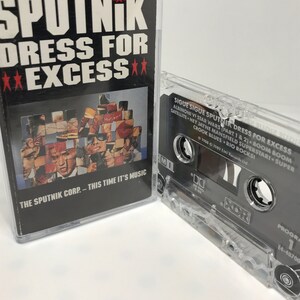 May include: A black cassette tape with a clear plastic case. The tape is labeled "Sputnik Dress for Excess" and features the text "SIGUE SIGUE SPUTNIK DRESS FOR EXCESS" and "THE SPUTNIK CORP. - THIS TIME IT'S MUSIC".