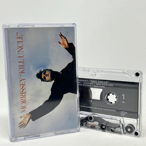 Puede incluir: Dos cintas de cassette vintage. La primera cinta presenta la portada del álbum "Kill Uncle" de Morrissey con una foto de Morrissey. La segunda cinta muestra la lista de canciones y el número 1.