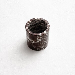 May include: A cylindrical container with a marble pattern in shades of brown and white. The container is a solid, sturdy design, perfect for holding pens, pencils, or other small items. The background is a plain white surface.