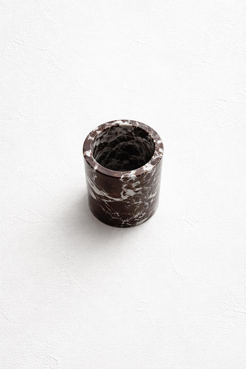 May include: A cylindrical container with a marble pattern in shades of brown and white. The container is a solid, sturdy design, perfect for holding pens, pencils, or other small items. The background is a plain white surface.