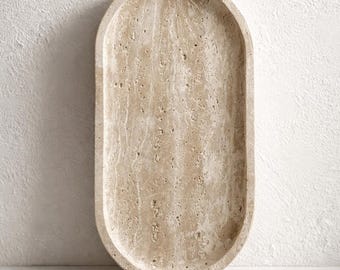 May include: Oval-shaped beige stone tray with a textured surface. The tray has rounded edges and a smooth interior. The neutral color and natural material suggest a decorative or functional item for home decor.