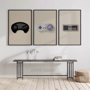 Könnte beinhalten: Drei gerahmte Drucke mit minimalistischen Illustrationen klassischer Videospiel-Controller. Die Controller sind schwarz, grau und lila, vor einem neutralen Hintergrund. Die Rahmen sind schwarz, für einen modernen und Retro-Look.