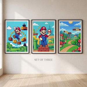 Peut inclure: Un ensemble de trois affiches encadrées représentant des scènes de jeux vidéo pixélisées. La première montre un personnage sautant vers des pièces, la deuxième le personnage tenant un champignon sur une brique, et la troisième un paysage.