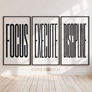 May include: Three framed art prints with black text on a white background. The prints read "FOCUS", "EXECUTE", and "DISCIPLINE". The frames are black, and the prints are displayed on a white wall above a wooden floor.