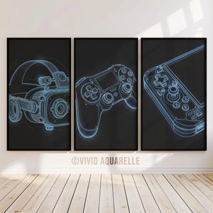 May include: Three framed art prints with neon blue line drawings of gaming devices on a black background. The prints show a VR headset, a game controller, and a handheld gaming console. The prints are displayed on a white wall above a wooden floor.
