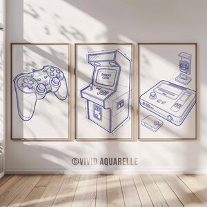 Könnte beinhalten: Drei gerahmte Drucke mit blauen Strichzeichnungen von Spielekonsolen und Zubehör. Die Drucke zeigen einen Gamecontroller, einen Spielautomaten mit dem Text "INSERT COIN" und eine Konsole mit einer Spielkassette. Das Kunstwerk befindet sich auf weißem Hintergrund.