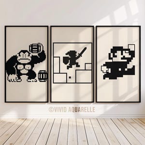 Peut inclure: Ensemble de trois impressions encadrées présentant des personnages de jeux vidéo classiques en pixel art : Donkey Kong, un chevalier avec une épée et Mario. Les illustrations en noir et blanc sont sur fond crème, avec un cadre noir. Les impressions sont affichées sur un mur blanc.