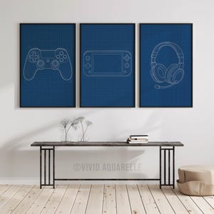 Könnte beinhalten: Drei gerahmte Drucke mit weißen Strichzeichnungen von Gaming-Zubehör auf blauem Rasterhintergrund. Die Drucke zeigen einen Gamecontroller, eine Handheld-Konsole und ein Headset. Die Rahmen sind schwarz.