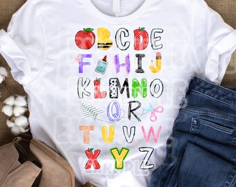 May include: White t-shirt with a colorful alphabet design featuring various school supplies and a red apple. The letters are outlined in black and have a hand-drawn style.