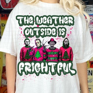 May include: White t-shirt with a green and pink graphic design featuring four horror movie characters wearing Christmas sweaters. The text reads "The weather outside is frightful".
