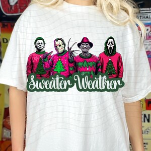 May include: White t-shirt with a graphic of four horror movie characters wearing Christmas sweaters. The characters are Michael Myers, Jason Voorhees, Freddy Krueger, and Ghostface. The text "Sweater Weather" is written below the characters.