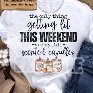 以下が含まれることがあります： 「the only thing getting lit THIS WEEKEND -are my fall- scented candles」の文字が入った白いTシャツ。秋をテーマにしたラベルが付いた3つのアロマキャンドルのイラストが特徴です。青いジーンズとタンブーツも写っています。