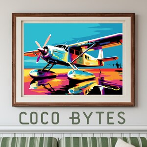 May include: Colorful pop art style print of a seaplane on water, framed in a brown wooden frame. The artwork features a vibrant palette of blues, yellows, oranges, and purples. The text "COCO BYTES" is printed in green at the bottom.