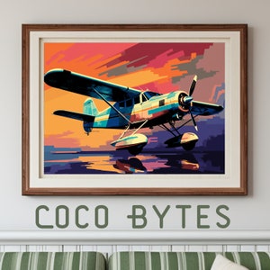May include: A framed art print featuring a colorful illustration of a seaplane in flight. The artwork showcases a vibrant sunset with shades of orange, pink, and purple. The seaplane is depicted in blue, white, and yellow. The text "COCO BYTES" is at the bottom.