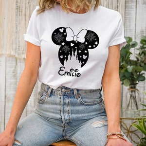Puede incluir: Camiseta blanca con un gr&aacute;fico en blanco y negro de orejas de Mickey Mouse con un lazo, fuegos artificiales y un castillo en el interior. El texto "Emilio" est&aacute; impreso debajo del gr&aacute;fico.