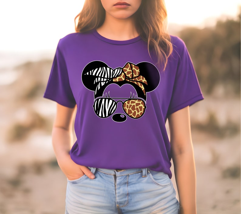 May include: Purple t-shirt with a graphic of a cartoon animal wearing sunglasses. The animal's ears are zebra and giraffe print, and the sunglasses are zebra and giraffe print.