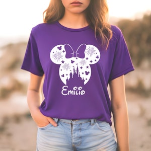 Puede incluir: Camiseta morada con una silueta blanca de orejas de Mickey Mouse, un lazo, fuegos artificiales, un castillo y estrellas. El texto "Emilio" est&aacute; debajo del dise&ntilde;o.