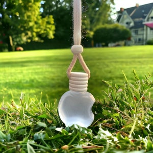 May include: A white apple-shaped car air freshener with a string for hanging. The air freshener is hanging from a white string.