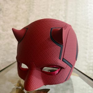 May include: A red plastic Daredevil mask with black accents and horns. The mask has a textured surface and eye holes.