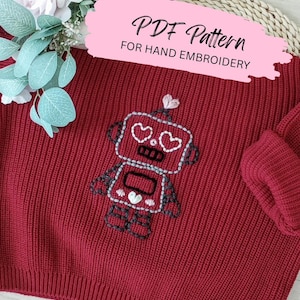 May include: A red knit sweater with a hand-embroidered robot design. The robot has heart-shaped eyes and a heart on its head. The text "PDF Pattern for Hand Embroidery" is displayed on a pink banner.