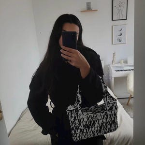 May include: A rectangular handbag featuring a thick, chunky knit texture with a high-contrast black and white marbled pattern. The bag includes two integrated top handles and a small rectangular brand label attached to the front surface.