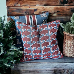 May include: Two decorative throw pillows with a blue and white striped pattern and a red and blue buffalo pattern. The pillows are on a wooden surface.