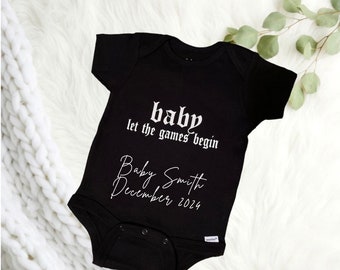 May include: Black baby onesie with white text that reads "baby let the games begin" and "Baby Smith December 2024".