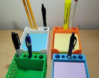 May include: Four colorful desk organizers, each with a different color: white, orange, green, and blue. Each organizer holds a stack of sticky notes and has holes for pens and pencils. Pencils, pens, and a highlighter are in the organizers.