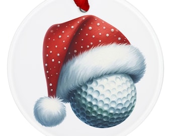 Puede incluir: Adorno navideño redondo y blanco con una pelota de golf que lleva un gorro de Papá Noel. El gorro rojo tiene lunares blancos y un ribete blanco y esponjoso. Se adjunta una cinta roja para colgarlo.