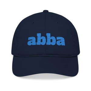 May include: A navy blue baseball cap with the word "abba" embroidered in light blue across the front. The cap has a curved brim and a structured crown, suitable for casual wear.