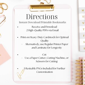 May include: A pink clipboard with gold hardware holds a white paper with instructions for printable bookmarks. The text includes directions for downloading, printing, and cutting. Gold scissors, paper clips, and a pen are scattered around the clipboard.