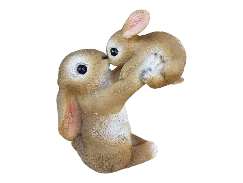 May include: A brown bunny figurine holding a smaller bunny. The larger bunny is lifting the smaller bunny up, with their noses touching. The figurine has large, dark eyes and pink accents on the ears.