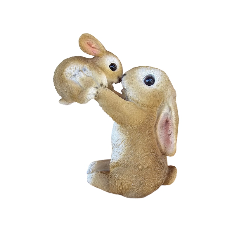 May include: A light brown bunny figurine holding a smaller bunny. The larger bunny is sitting with its legs tucked under, holding the smaller bunny up to its face. The bunnies have large black eyes and pink inner ears.