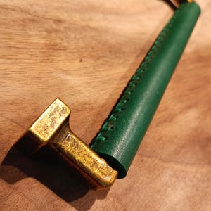 May include: A green leather pull handle with a gold metal base. The handle is stitched with a decorative pattern.