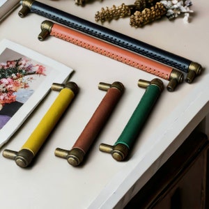 May include: Four different cabinet pulls with leather straps and brass accents. The pulls are yellow, brown, green, and black.