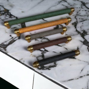 May include: Five different colored cabinet pulls with brass accents. The pulls are made of leather and have a variety of colors, including green, brown, gray, black, and orange.