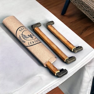 May include: Two brown leather drawer pulls with metal accents. The pulls are rolled up in a brown paper tube with the text "Gaffa Leather" printed on it.