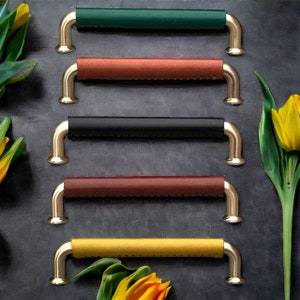 May include: Five different leather drawer pulls with gold metal hardware. The pulls are in various colours, including green, brown, black, red, and yellow.