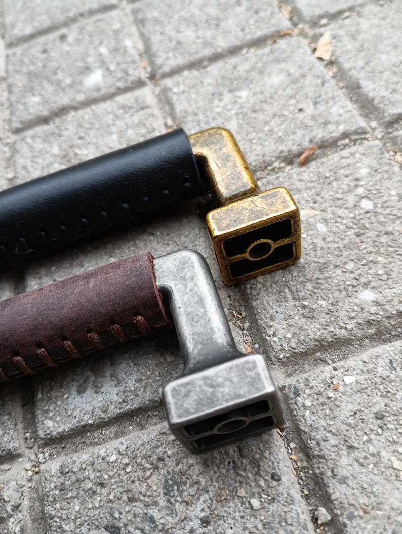 May include: Two leather wrapped handles with metal ends. The ends are square shaped with a round hole in the center. One handle is brown leather with a silver end and the other is black leather with a gold end.