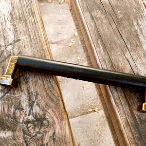 May include: A black leather handle with gold metal ends. The handle is on a wooden surface.