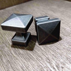 May include: Two silver-toned metal cabinet knobs with a square base and a pyramid-shaped top.