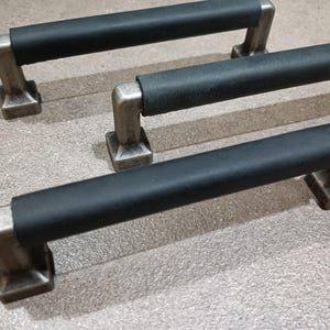 Peut inclure: Trois poignées de tiroir en cuir noir avec des bases en métal argenté. Les poignées sont rectangulaires et ont un bord arrondi.