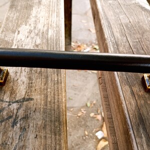 May include: Black metal door handle with gold accents. The handle is rectangular and has a smooth, flat surface.