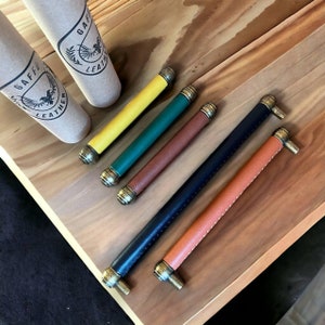 May include: Five leather drawer pulls with brass accents. The pulls are in the colours yellow, green, brown, black, and tan.